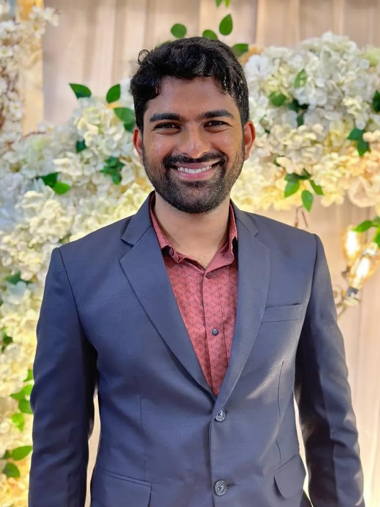 Man wearing a black suit and red shirt with a background having flowers